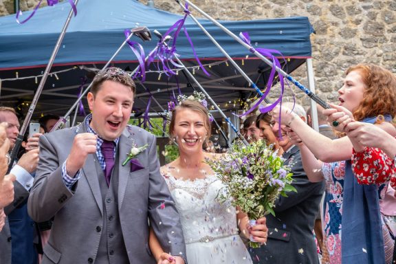 Smiling bride and groom celebrating with guests, surrounded by ribbons and flowers.