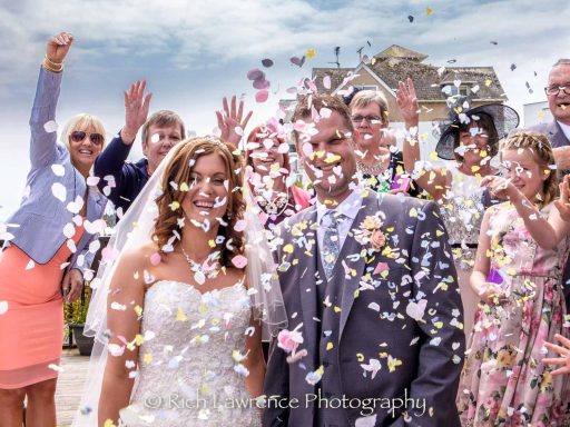 A bride and groom surrounded by guests throwing confetti at a wedding celebration.