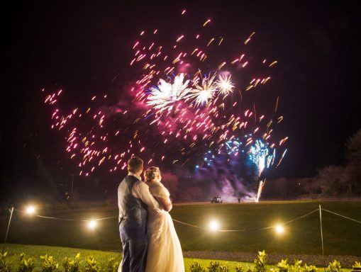 A couple embraces beneath a colourful fireworks display at night.