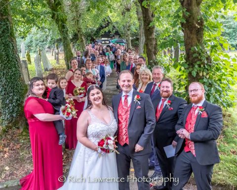 A wedding party posing together on a tree-lined path, smiling and holding bouquets.