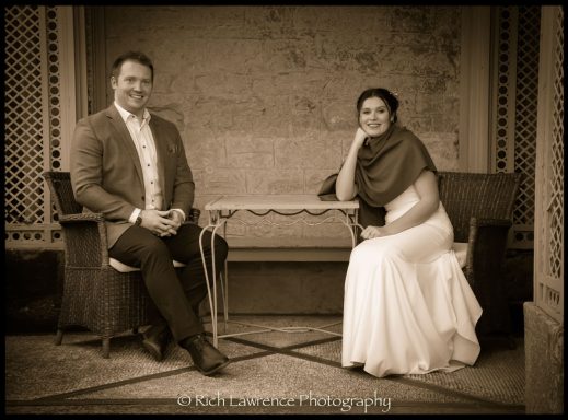 A man and woman seated together, smiling, with a decorative backdrop behind them.