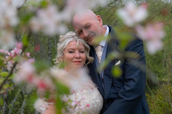 A bride and groom embrace surrounded by blooming flowers.