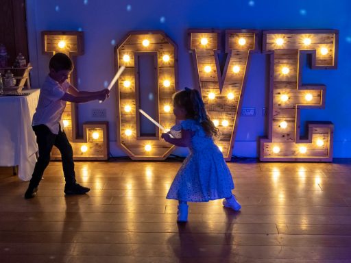 Two children play with light sabers in front of a large illuminated "LOVE" sign.