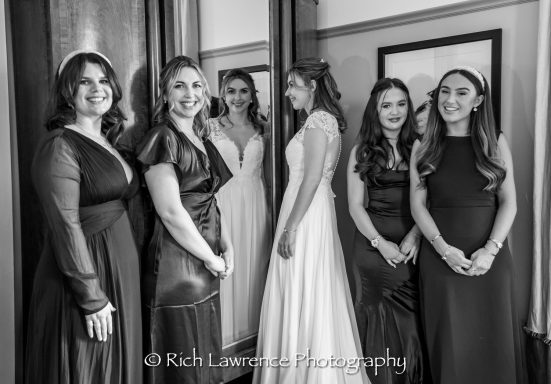 A bride in a white dress poses with five bridesmaids in elegant black dresses.