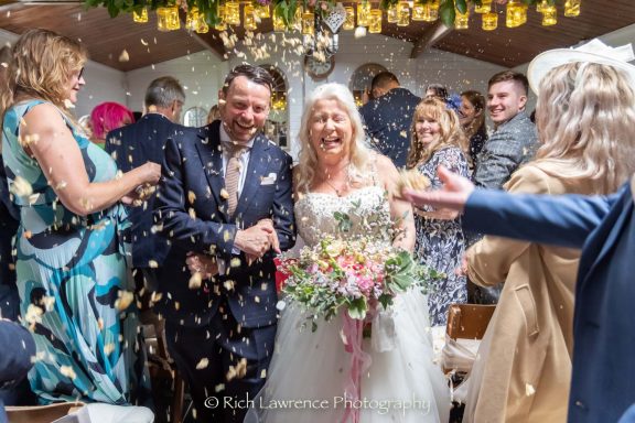 Wedding couple smiling and celebrating with confetti and joyful guests around them.