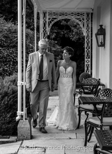 A bride in a wedding gown walking with a man in a suit along a garden pathway.