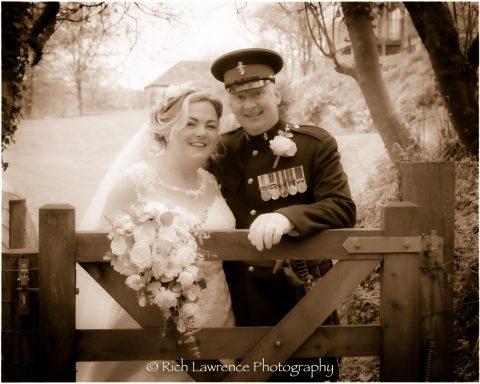 Bride and groom smiling together at a gate, in a sepia-toned setting.