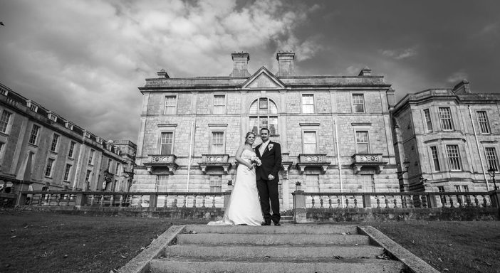 Bride and groom pose on steps in front of a historic building, captured in black and white.