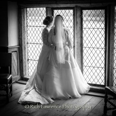 Two brides in elegant wedding attire gazing out of a window.