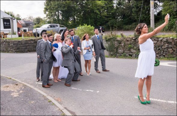 A woman in a white dress takes a selfie with a group of people wearing formal attire.