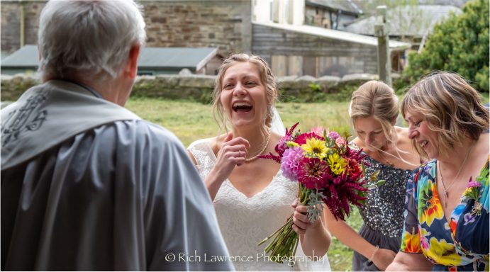 Bride laughing joyfully while holding a bouquet, surrounded by two women and a man.